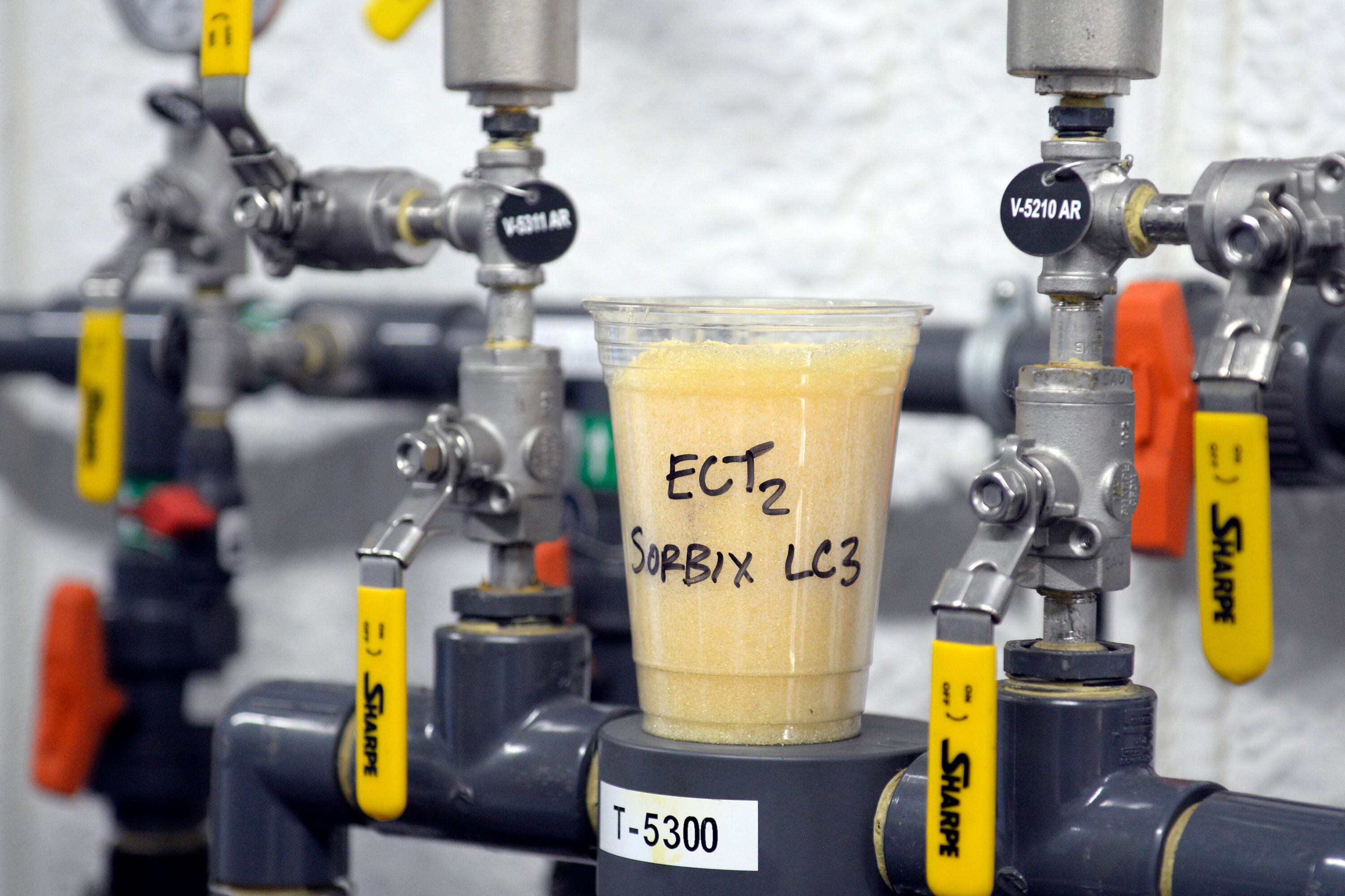 A cup full of single-use, ion-exchange, gel-based media sits atop valves that control a ground water remediation system being used to remediate polyfluoroalkyl substances (PFAS) from groundwater at the fire training area of Wright-Patterson Air Force Base, Ohio on Sept. 29, 2020.