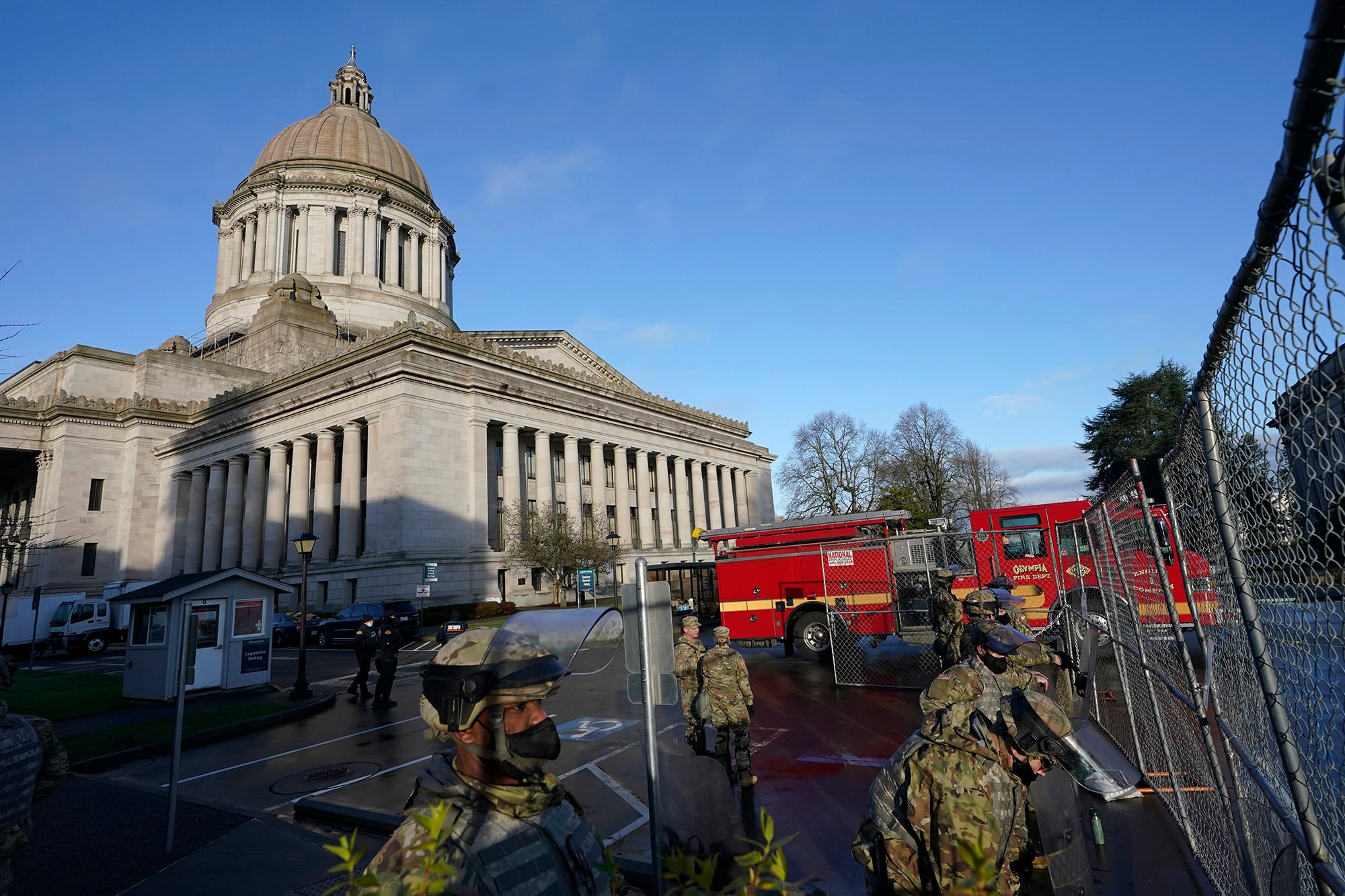 Members of the Washington National Guard stand along a perimeter fence as an Olympia Fire Dept. truck passes by, Sunday, Jan. 10, 2021, at the Capitol in Olympia, Wash.