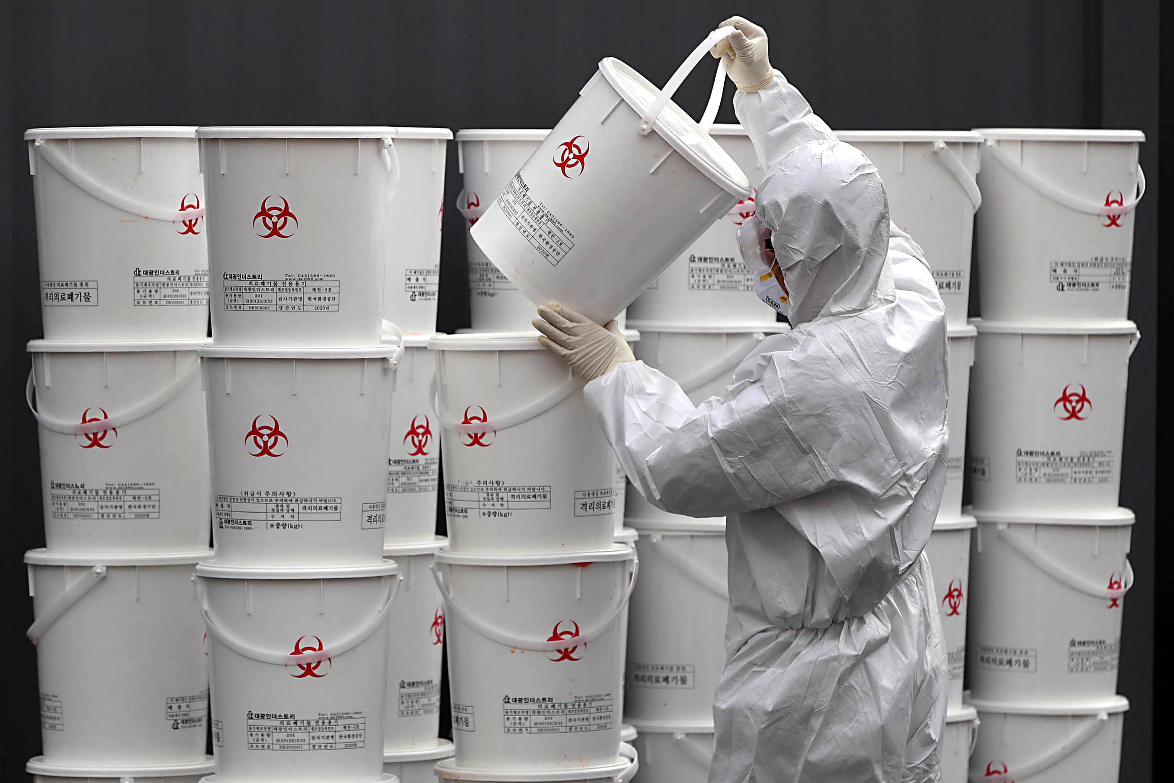 A worker in protective gear stacks plastic buckets containing medical waste from coronavirus patients at a medical center in Daegu, South Korea