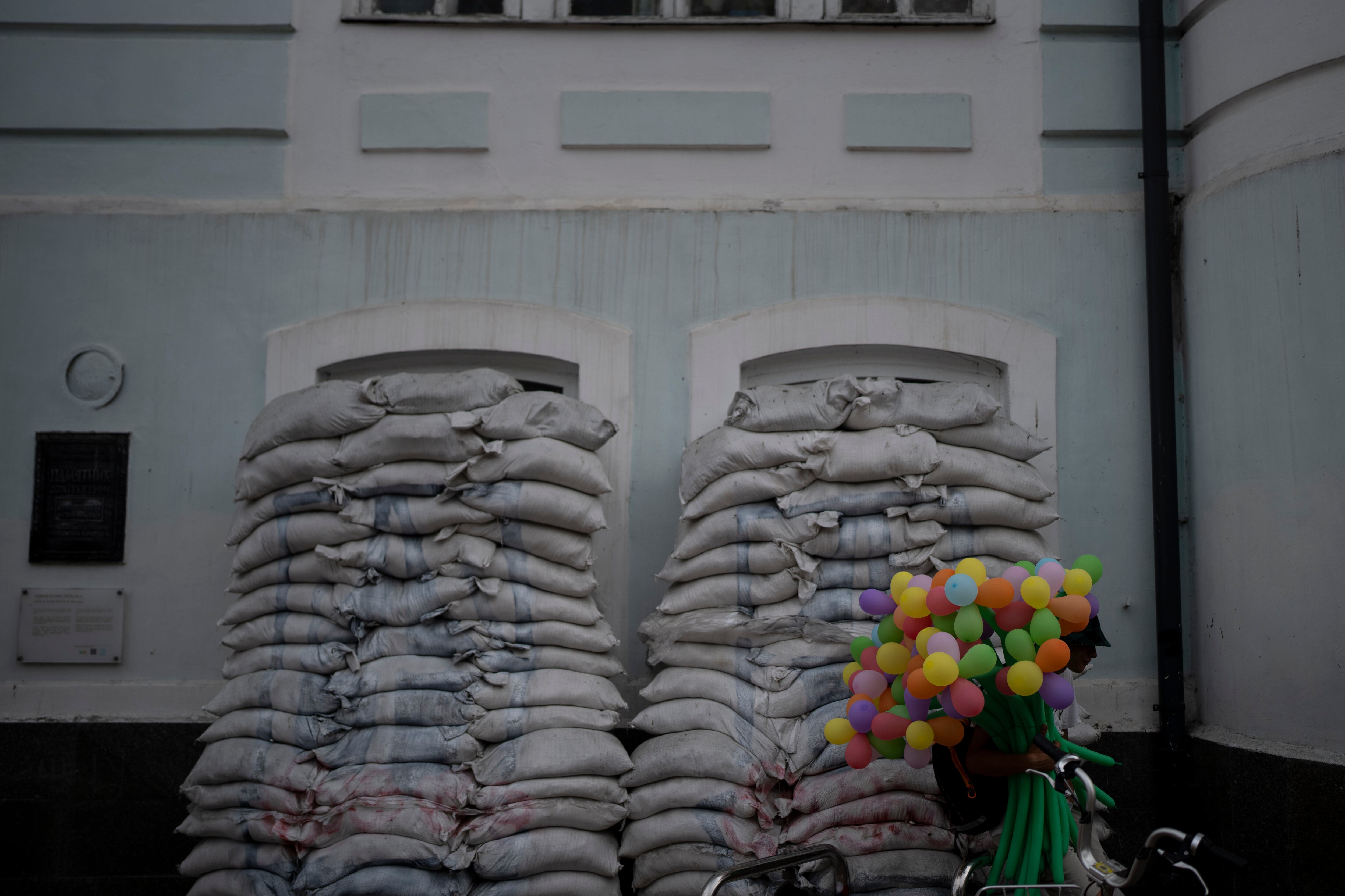 A man sells balloons next to piles of sandbags blocking windows of an old building in Kyiv, Ukraine, Saturday, Aug. 26, 2023.