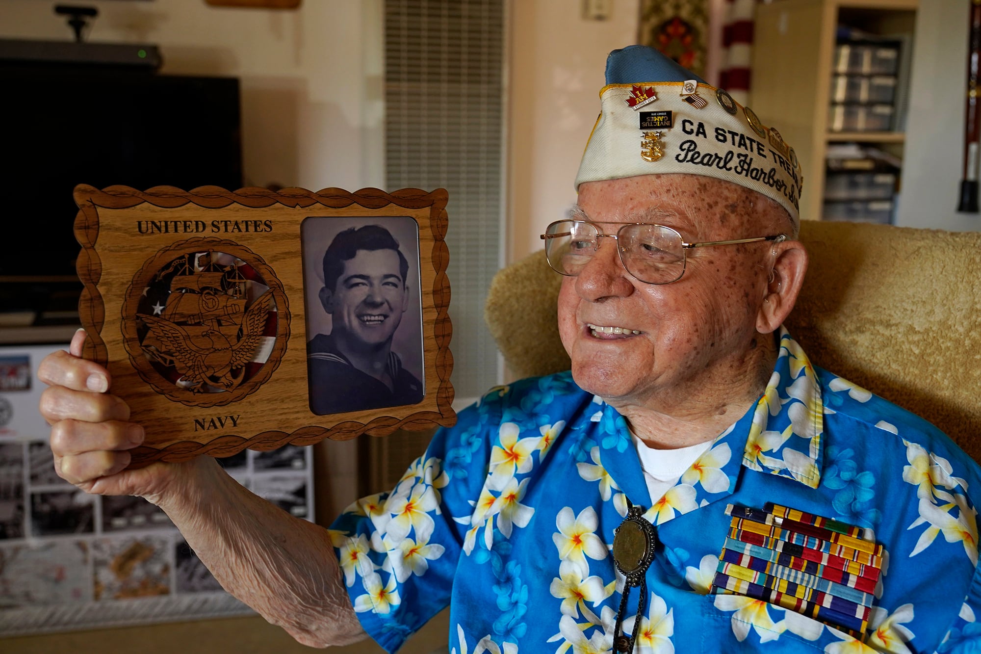 Mickey Ganitch, a survivor of the 1941 attack on Pearl Harbor, holds a plaque with a picture of himself as a young sailor, while sitting in the living room of his home in San Leandro, Calif. Nov. 20, 2020.