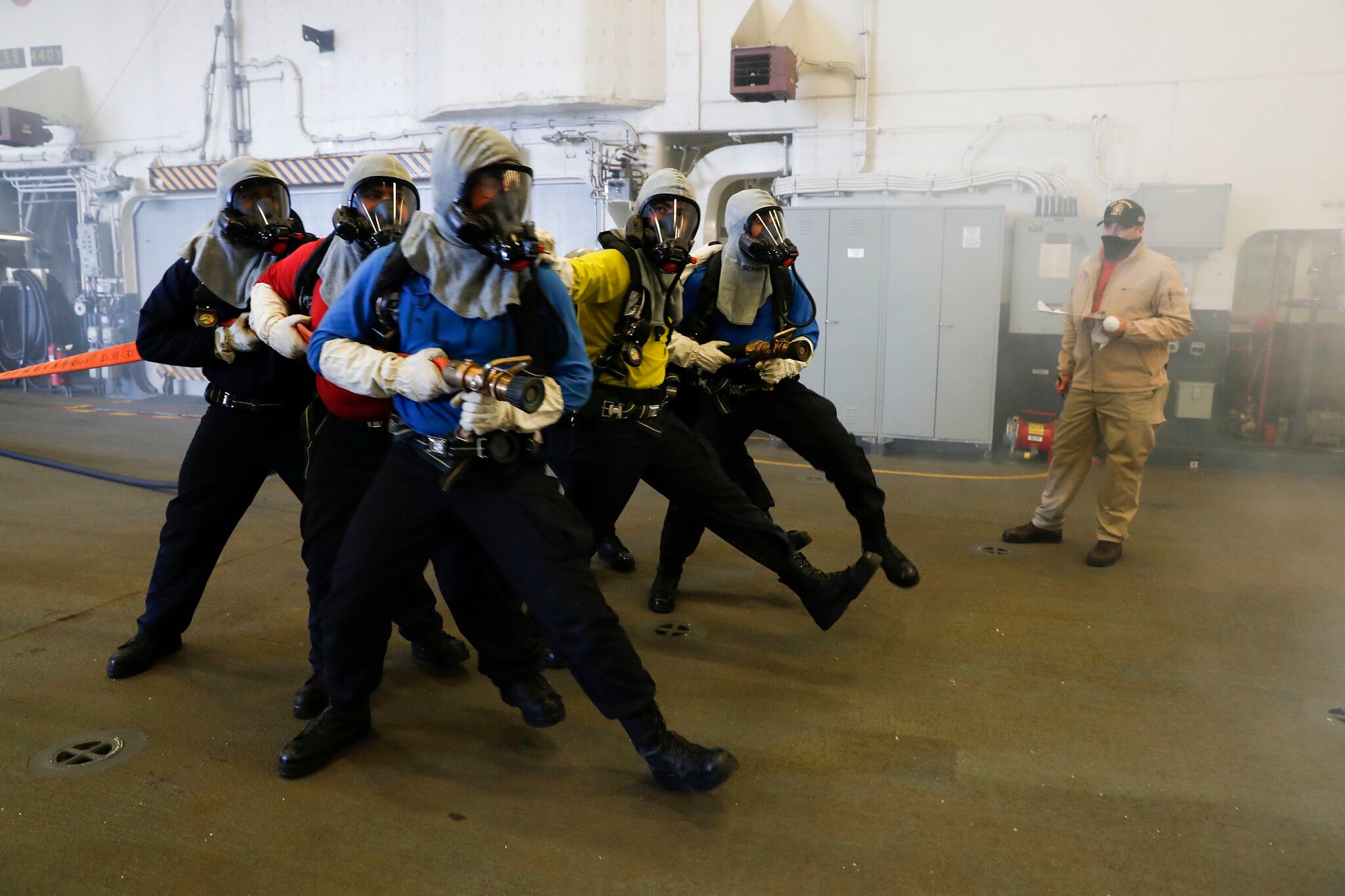 Aviation boatswain’s mates (handling) simulate approaching a fire during an aircraft firefighting drill in the hangar bay of the amphibious assault ship USS Tripoli (LHA 7), Aug. 31, 2020, in the Pacific Ocean.