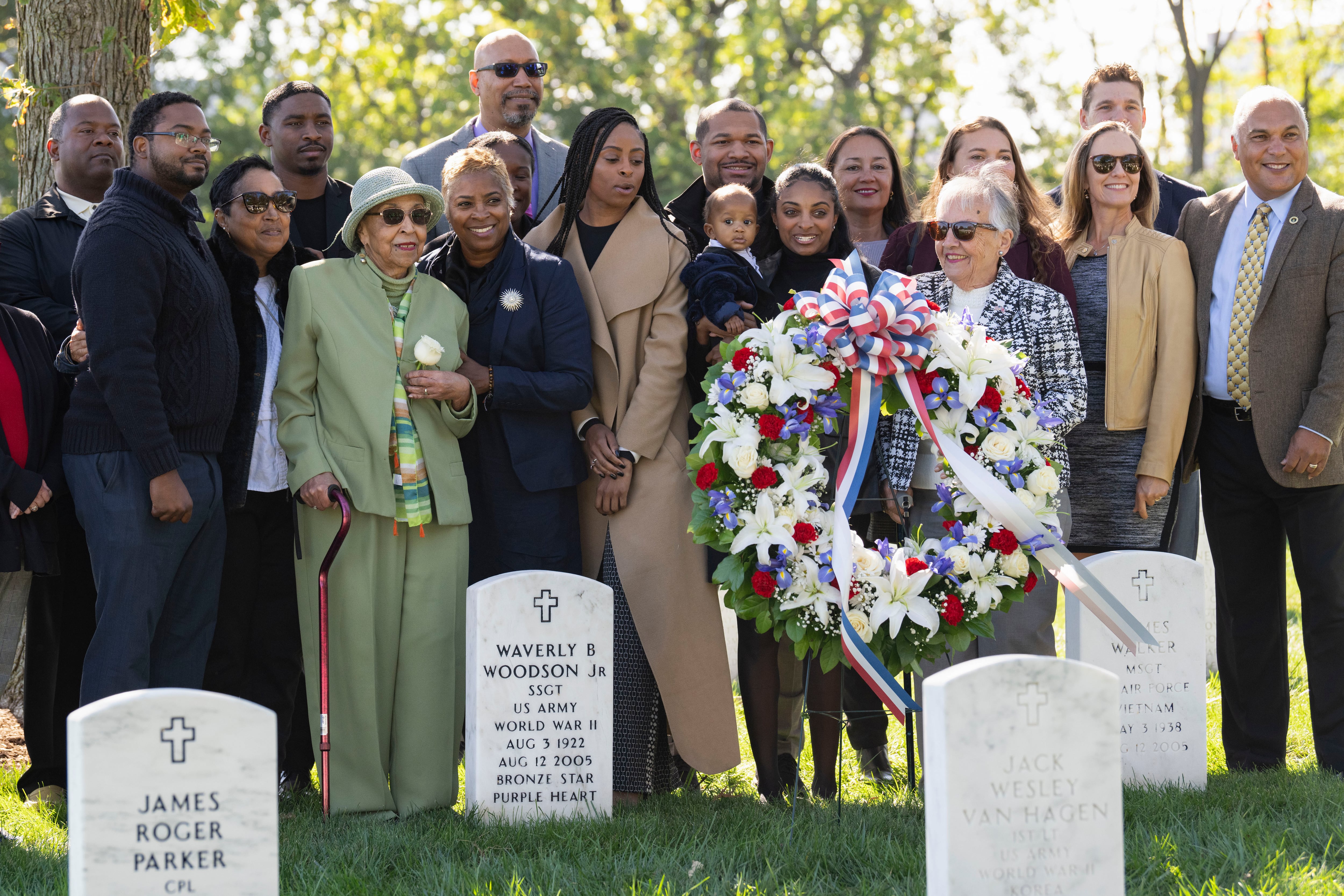 Joann Woodson, in green, is joined by family at the headstone of her husband, Cpl. Waverly B. Woodson Jr., following a ceremony at Arlington National Cemetery on Tuesday, Oct. 11, 2023 in Arlington, Va.