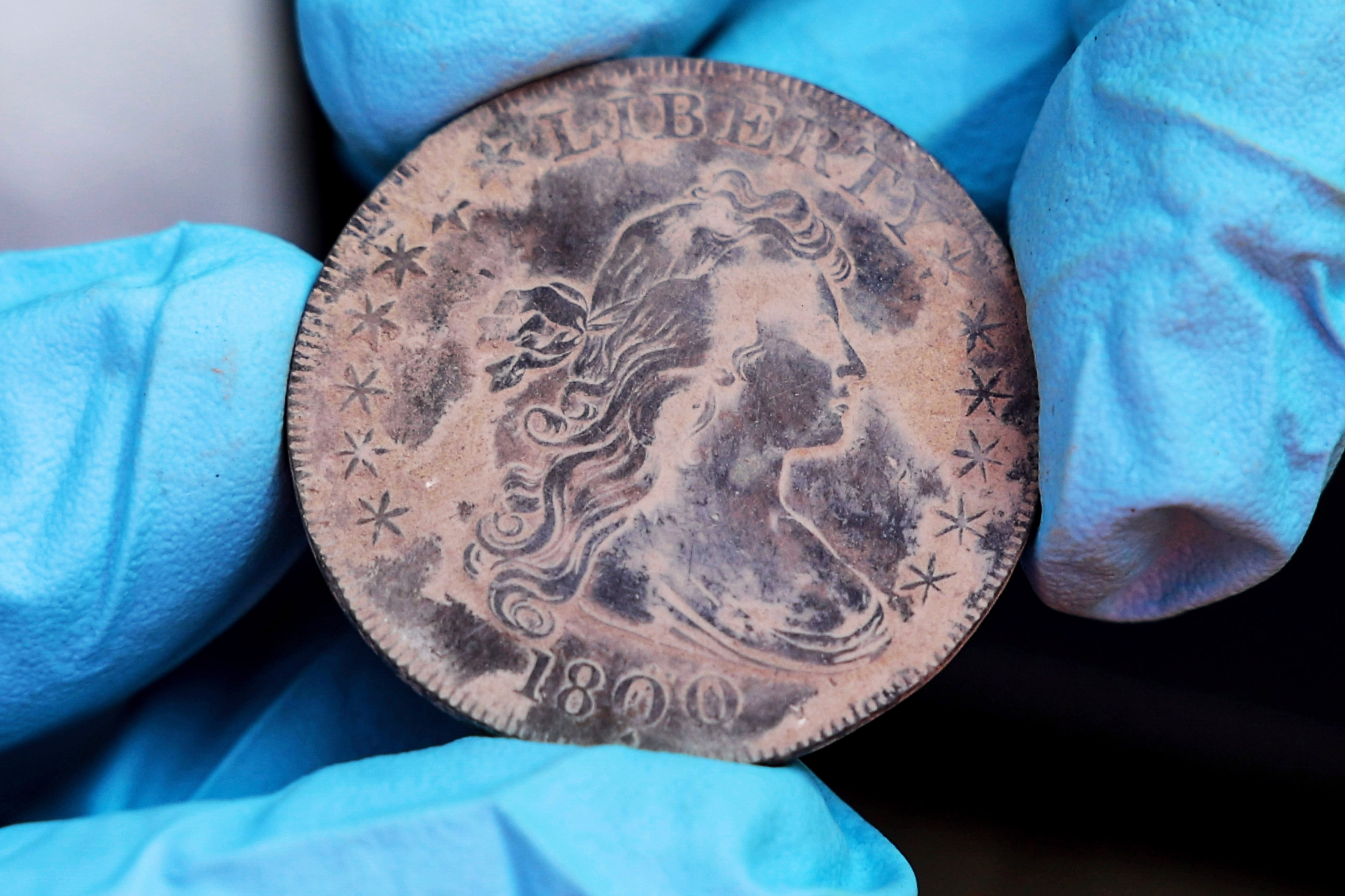 This photo, provided by the U.S. Military Academy at West Point, Aug. 30, 2023, shows West Point archeologist Paul Hudson display an 1800 Draped Bust Dollar, one of the coins found in the lead box believed to have been placed in the base of a monument by cadets almost two centuries ago, in West Point, NY.