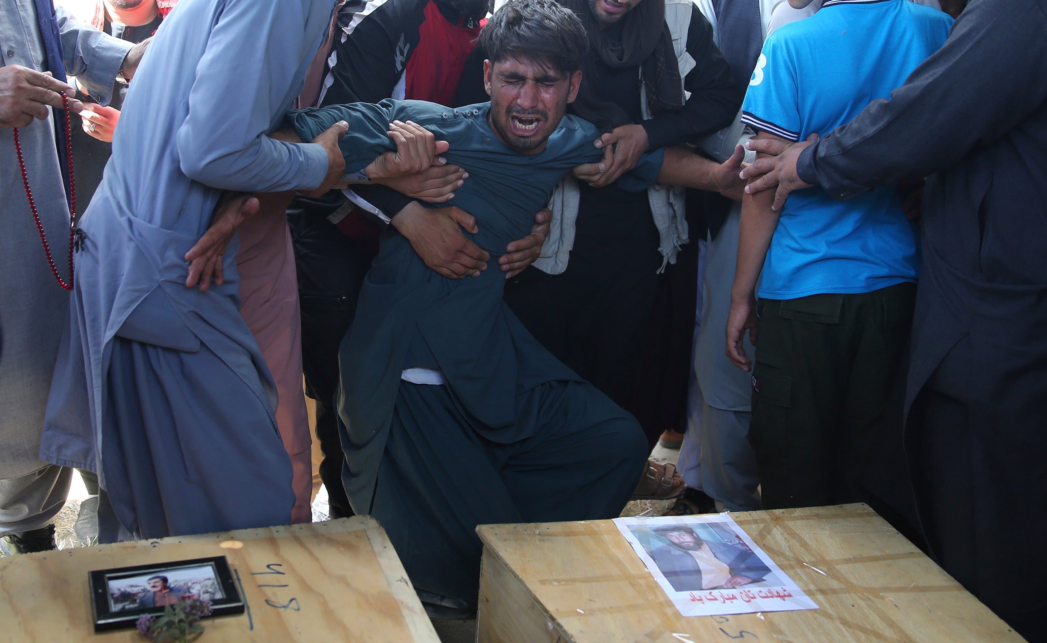 A relative wails near the coffins of victims of the Dubai City wedding hall bombing during a mass funeral in Kabul, Afghanistan, Sunday, Aug.18, 2019.